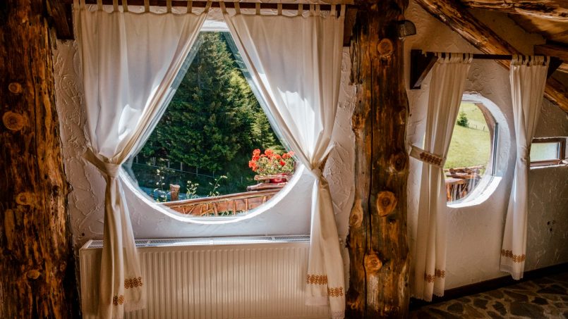 Camera rustică cu ferestre rotunde, detalii din lemn și vedere către natură