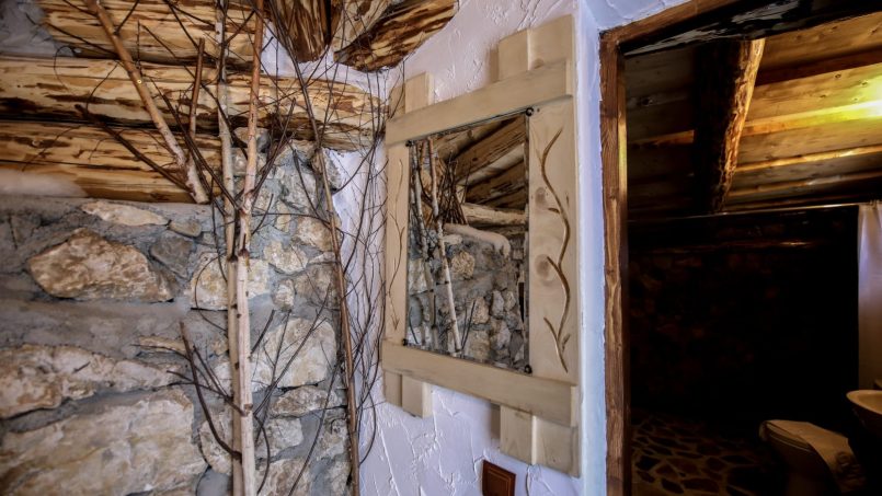 Coridor rustic cu perete din piatră, tavan din lemn și vedere către băie