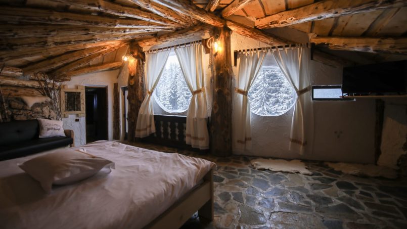 Camera rustică cu pat dublu, fereastra rotundă și podea din piatră