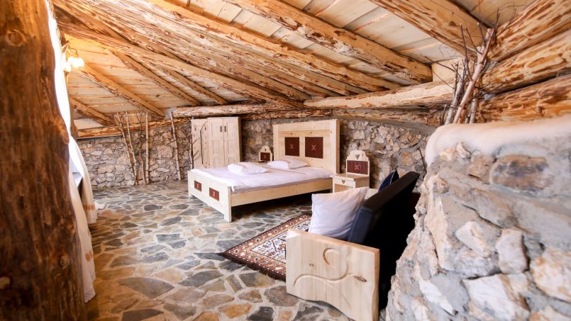 Camera rustică cu pat dublu, pereti din piatră, podea de pietre naturale și tavan din lemn