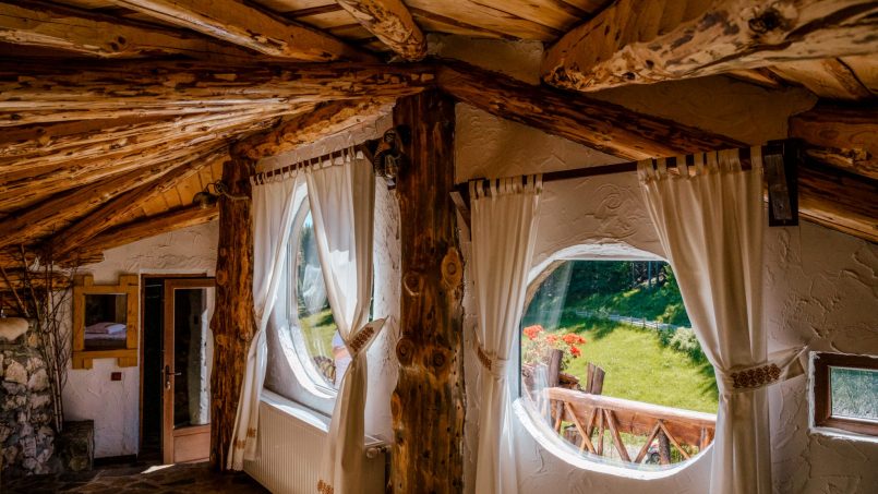 Interior rustic cu ferestre rotunde, perdele tradiționale și pereți din lemn