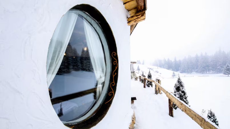 Round window in a snowy cottage with scenic mountain views