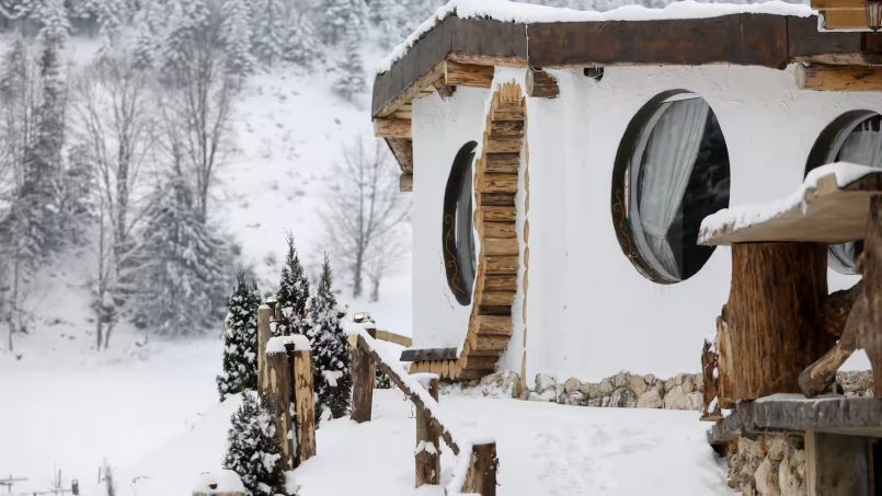 Snow-covered cottage featuring round windows and wooden accents